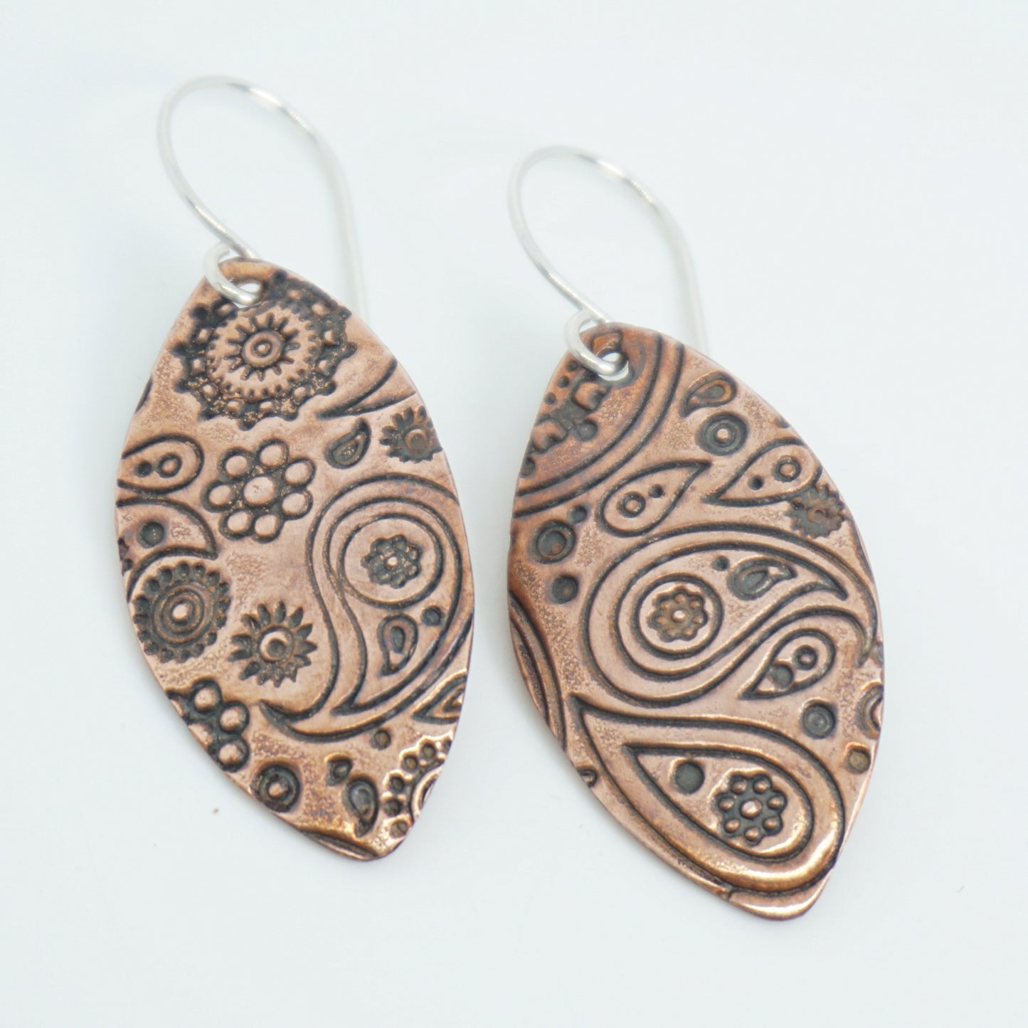 Pair of copper earrings with intricate patterns on a white background