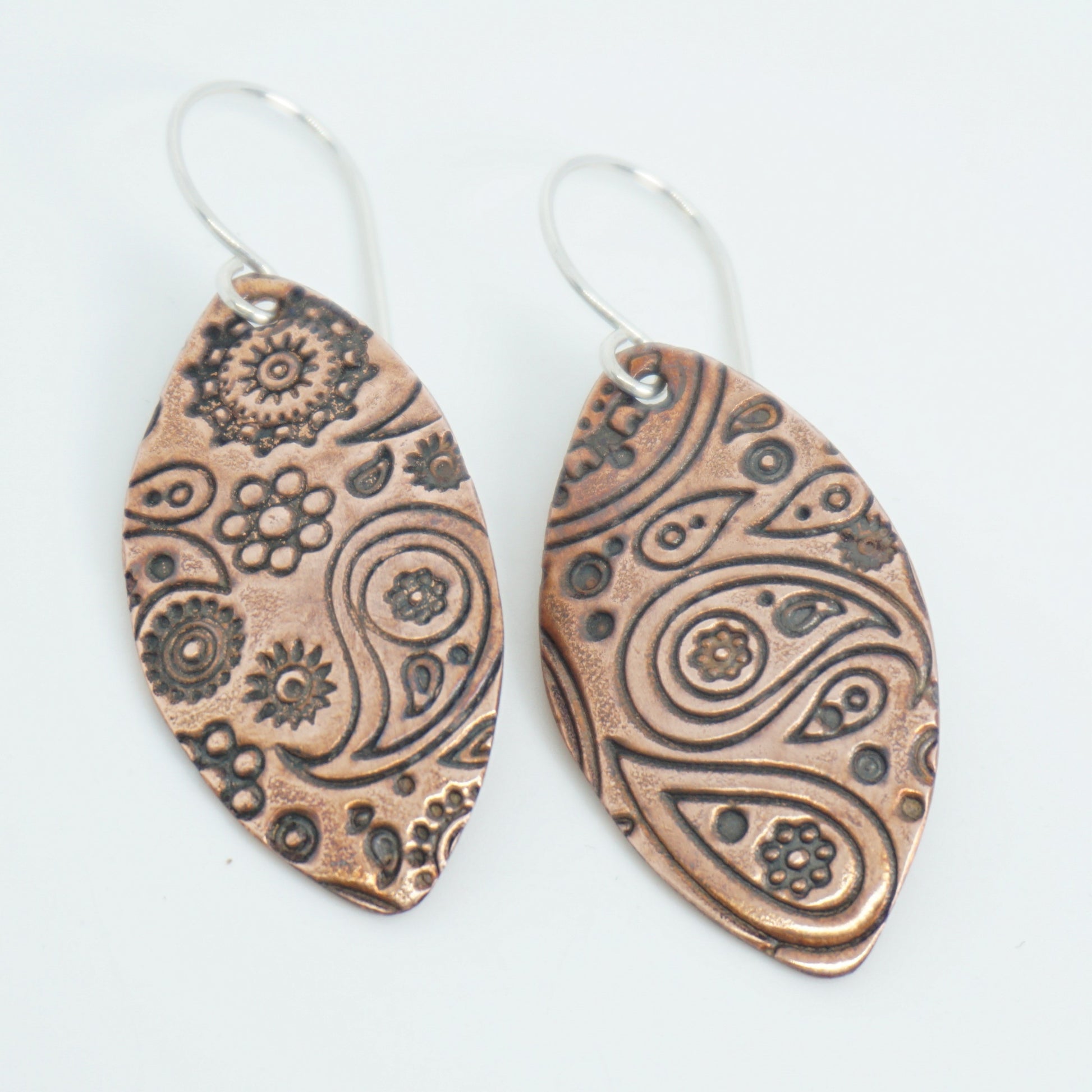 Pair of copper earrings with intricate patterns on a white background