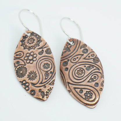 Pair of copper earrings with intricate patterns on a white background