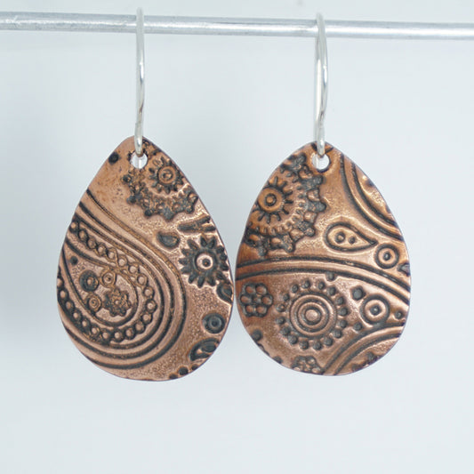 Teardrop-shaped copper earrings with intricate patterns on a white background