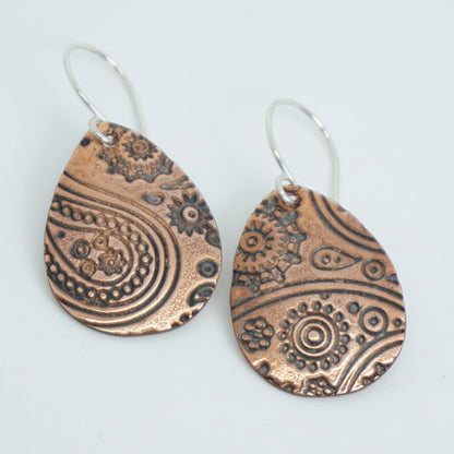 Pair of copper earrings with intricate patterns on a white background