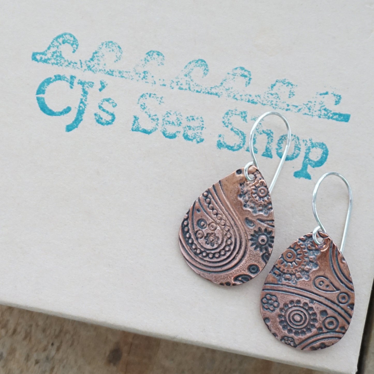 copper Teardrop-shaped earrings with intricate patterns on a gift box