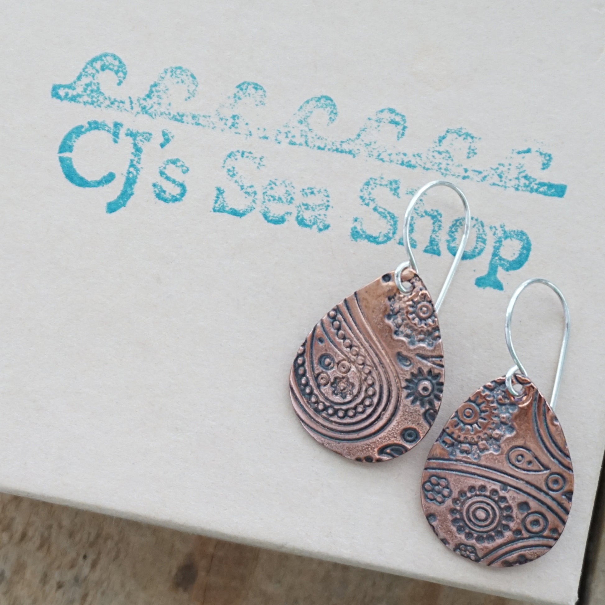 copper Teardrop-shaped earrings with intricate patterns on a gift box