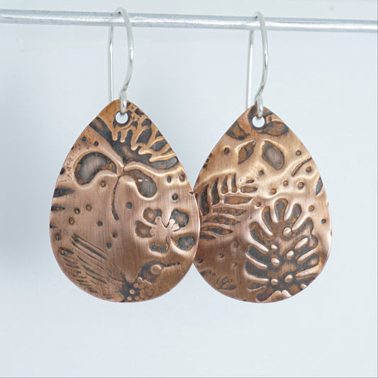 Pair of copper teardrop earrings with intricate patterns on a white background
