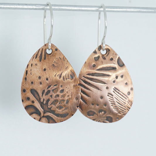 Pair of copper earrings with tropical patterns on a white background