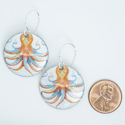 Pair of earrings with octopus design next to a penny for scale on a white background