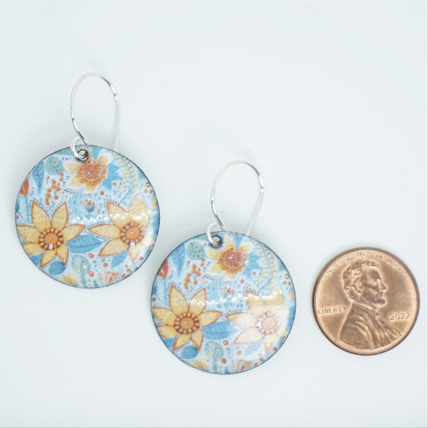 Floral patterned earrings with a penny for scale on a white background