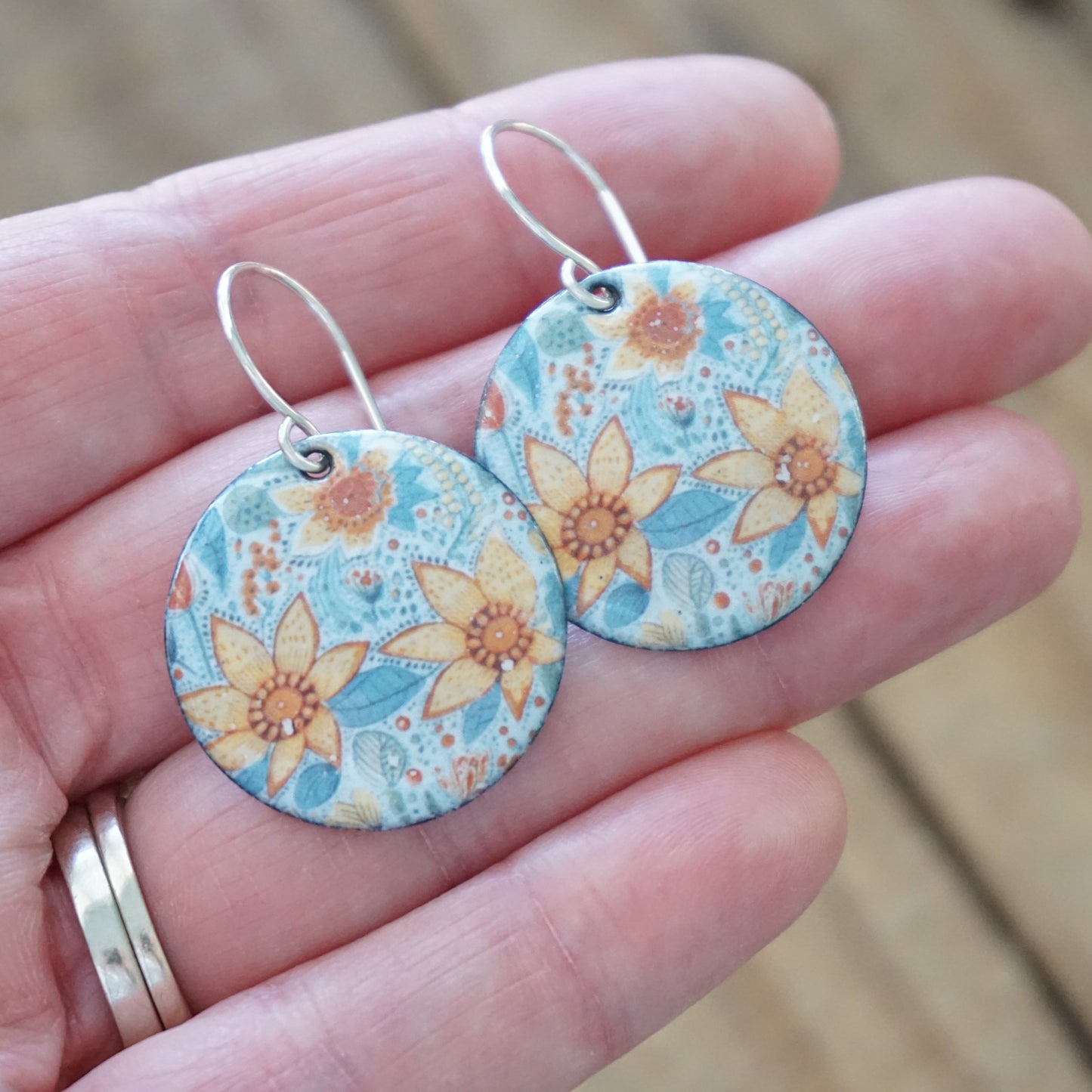 Floral patterned earrings held in a hand with a blurred background