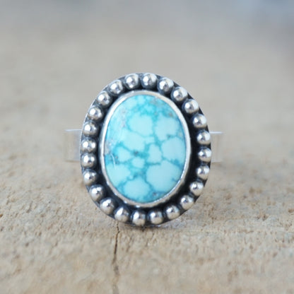 Turquoise ring with silver beaded trim on a wooden surface
