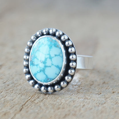 Turquoise stone ring with silver beaded border on a wooden surface