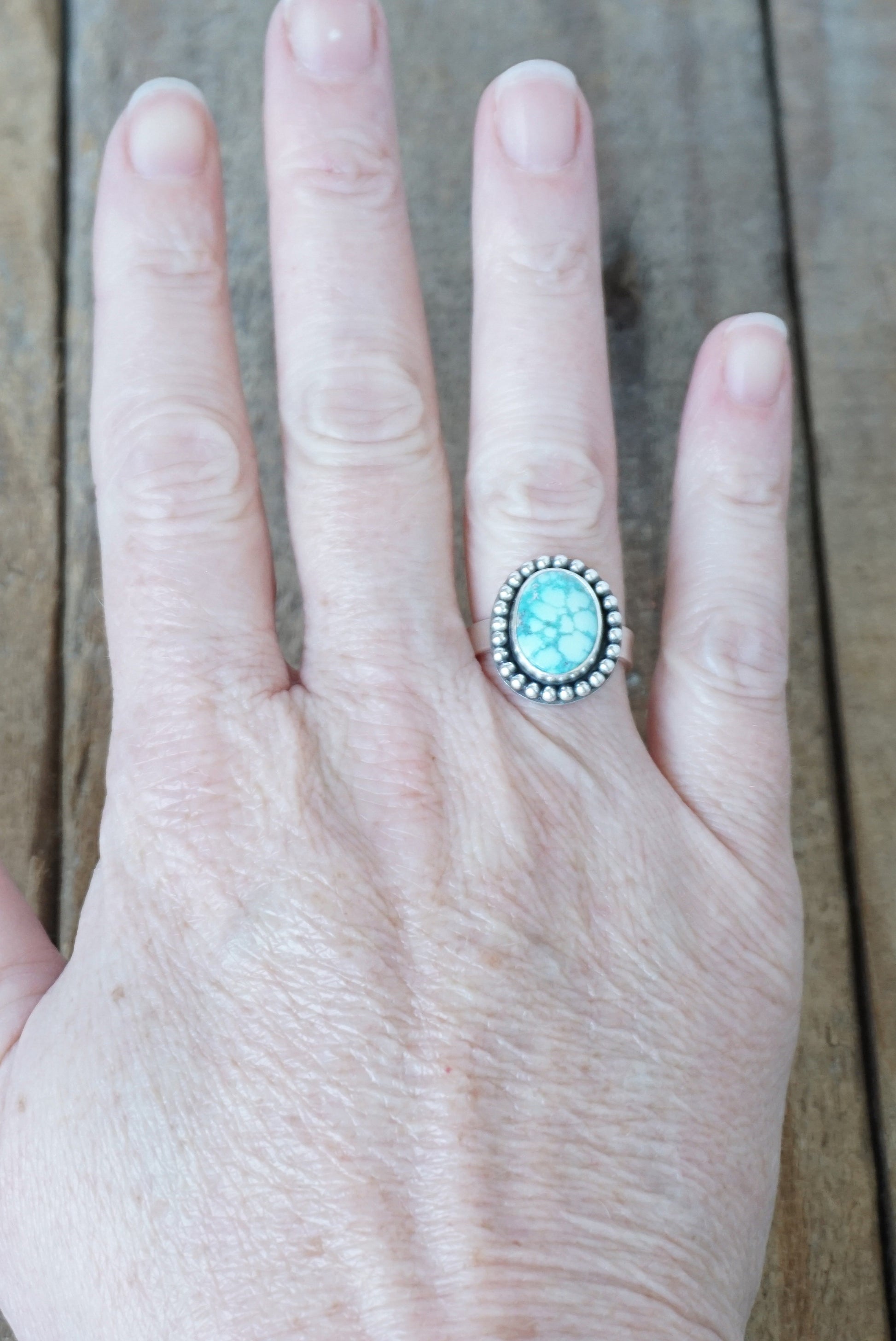 Hand wearing a ring with a turquoise stone on a wooden surface