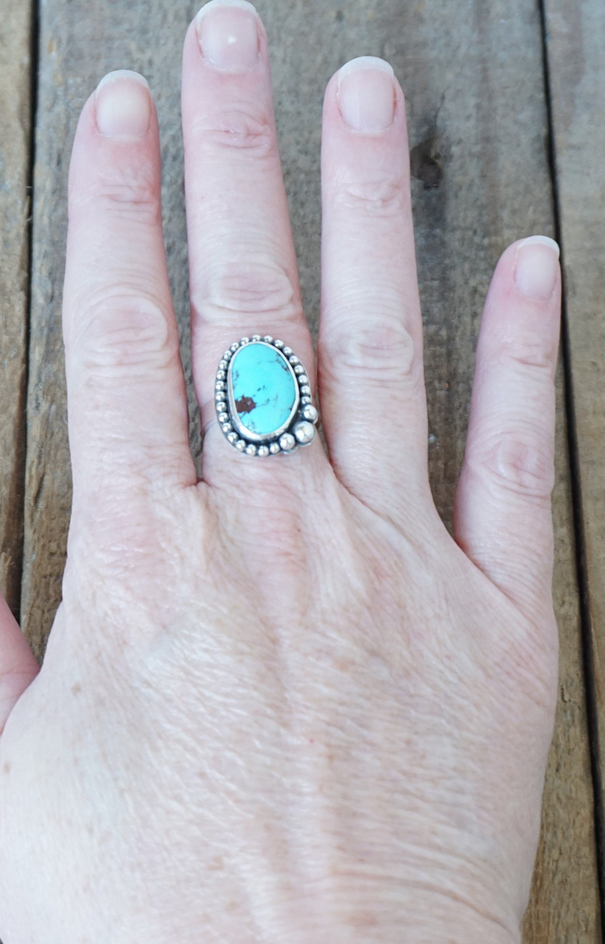 Turquoise ring on a hand with a wooden background