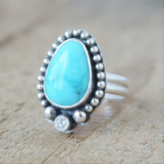Turquoise and silver ring, with bead detail and a clear cubic zirconia, against a wooden background