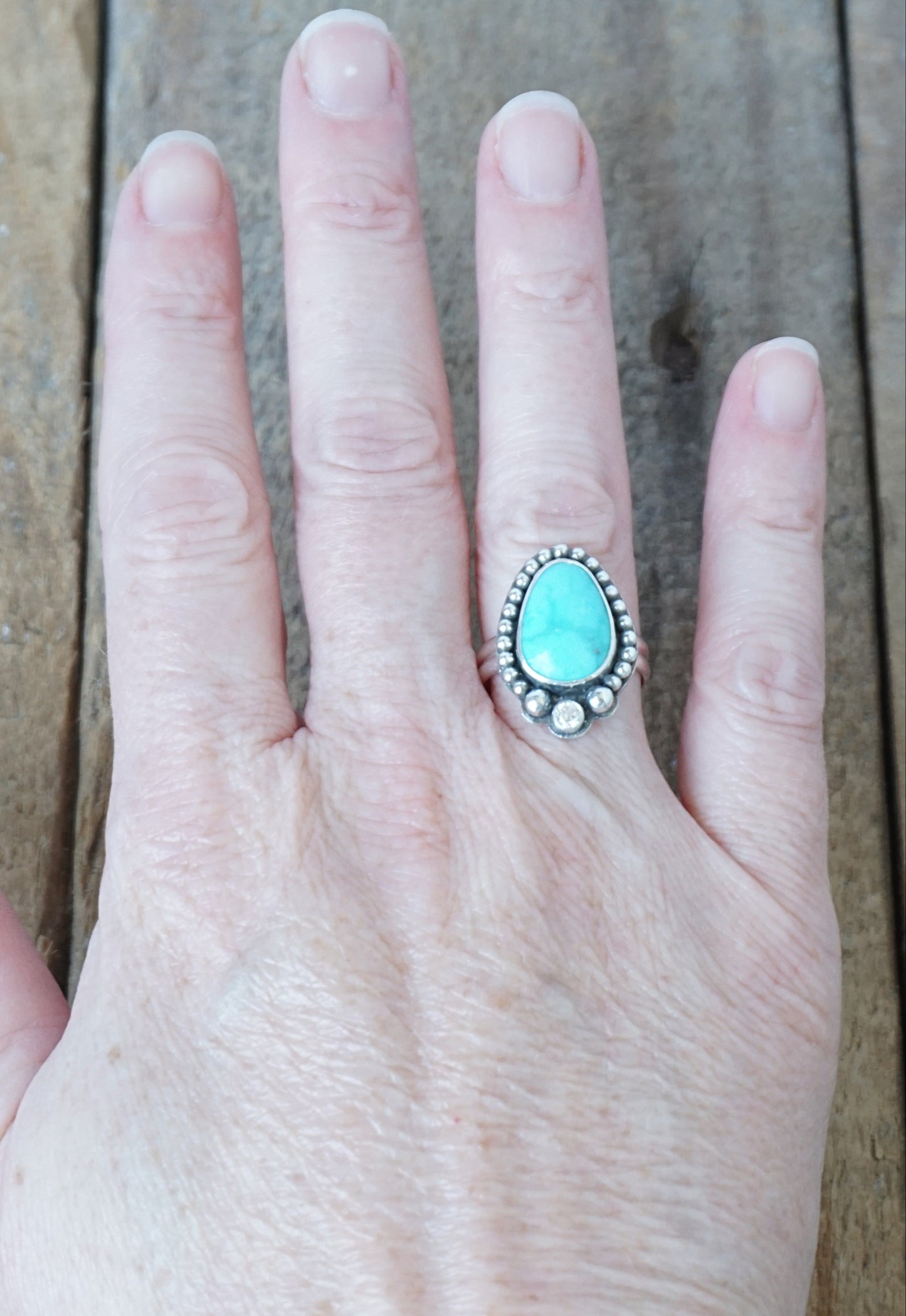 Hand wearing a turquoise stone ring on a wooden surface