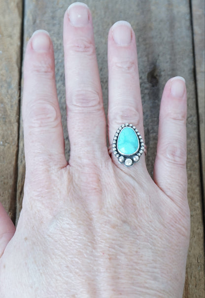 Hand wearing a turquoise stone ring on a wooden surface
