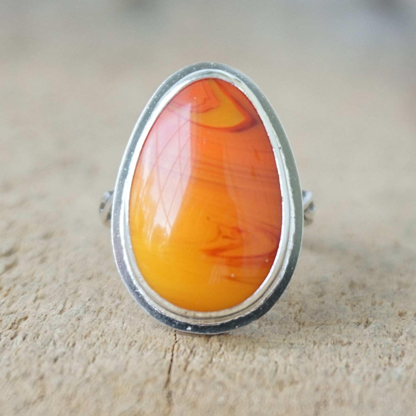 Silver ring with an orange stone on a wooden surface