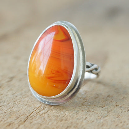 Silver ring with an orange stone on a wooden surface