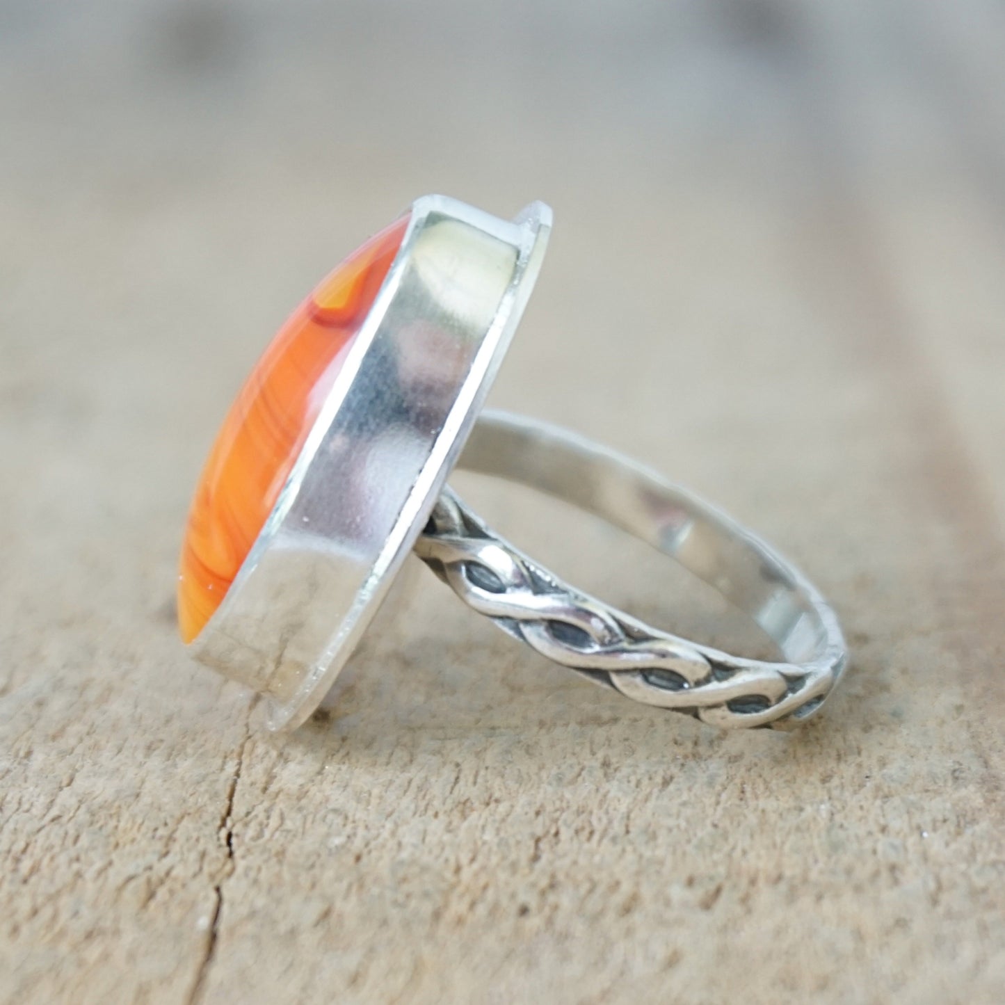side view of a Silver ring with an orange stone on a wooden surface