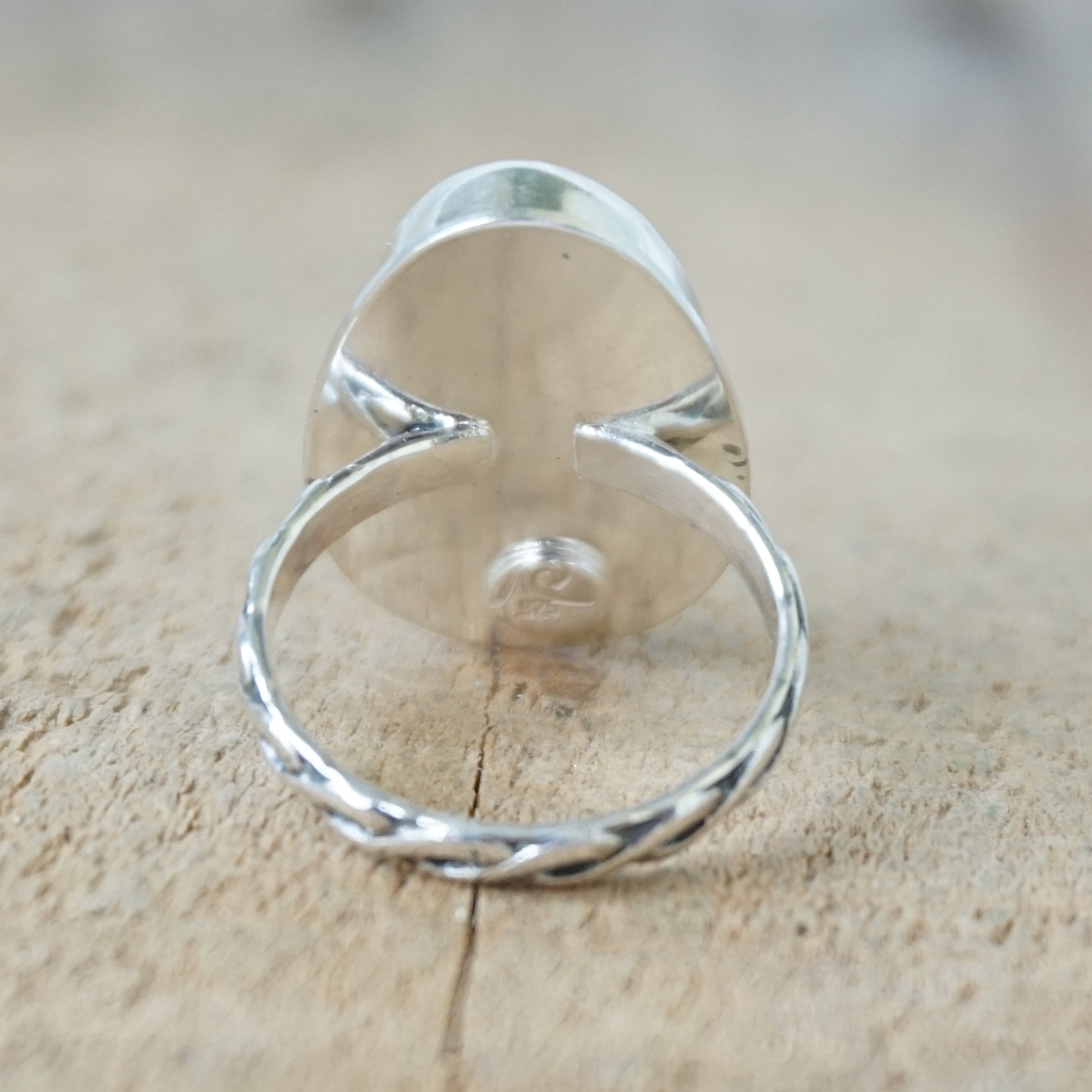 back view of a Silver ring with an orange stone on a wooden surface