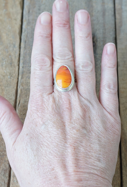 Hand wearing a ring with an orange stone on a wooden surface