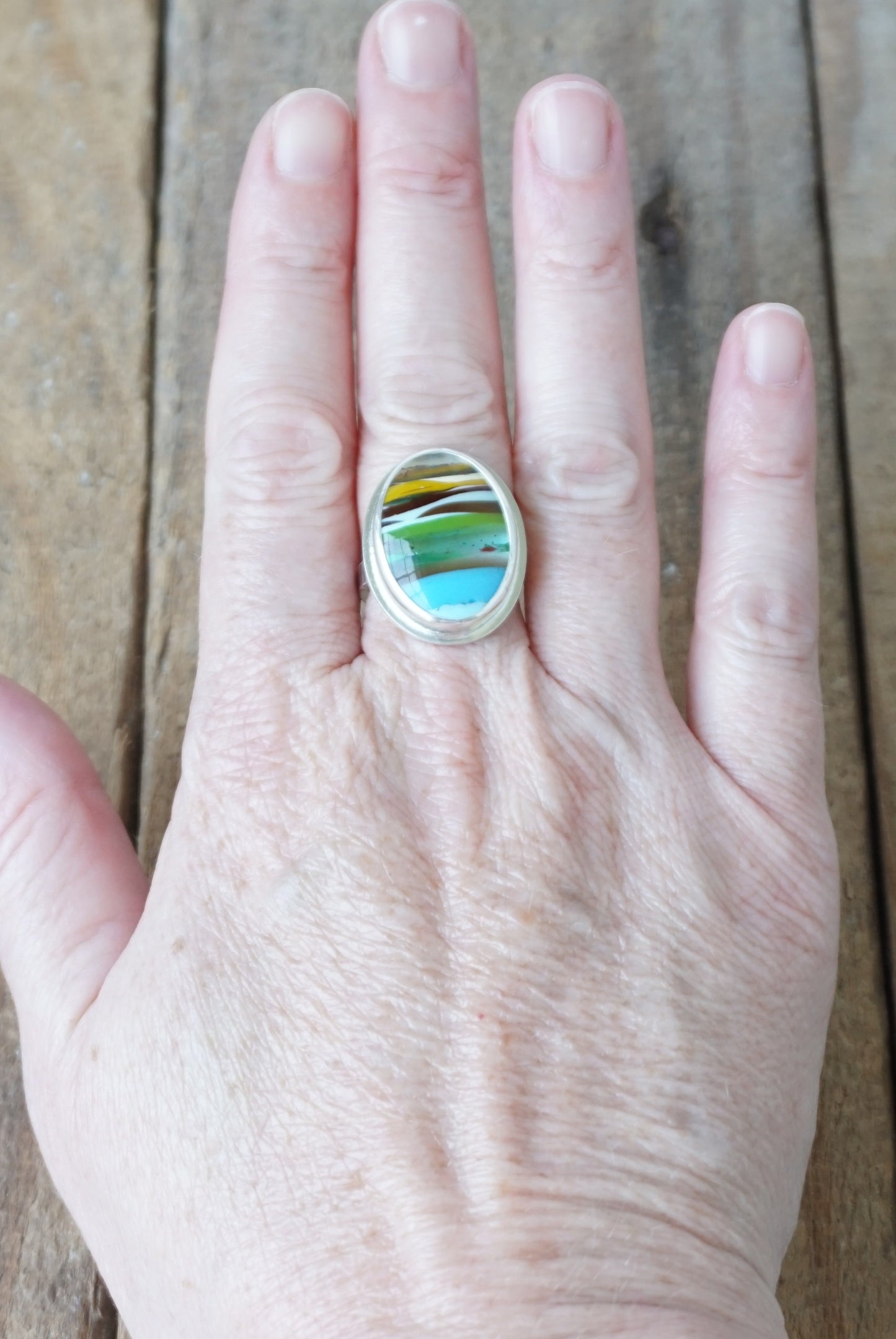 Hand wearing a ring with a colorful stone on a wooden surface