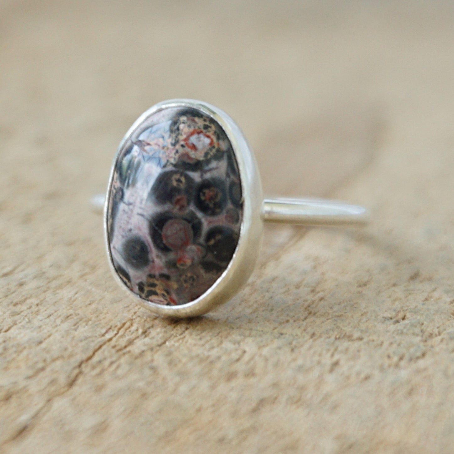 silver ring with a spotted stone on a wooden background