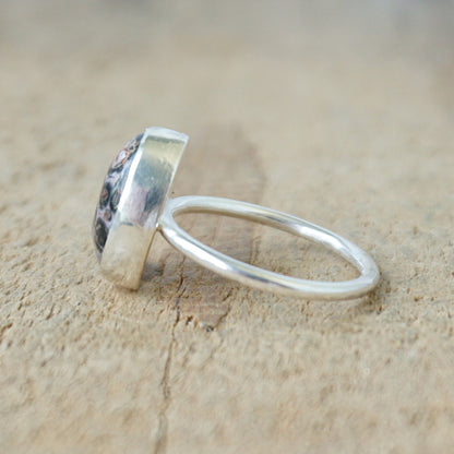 side view of a silver ring with a spotted stone on a wooden background