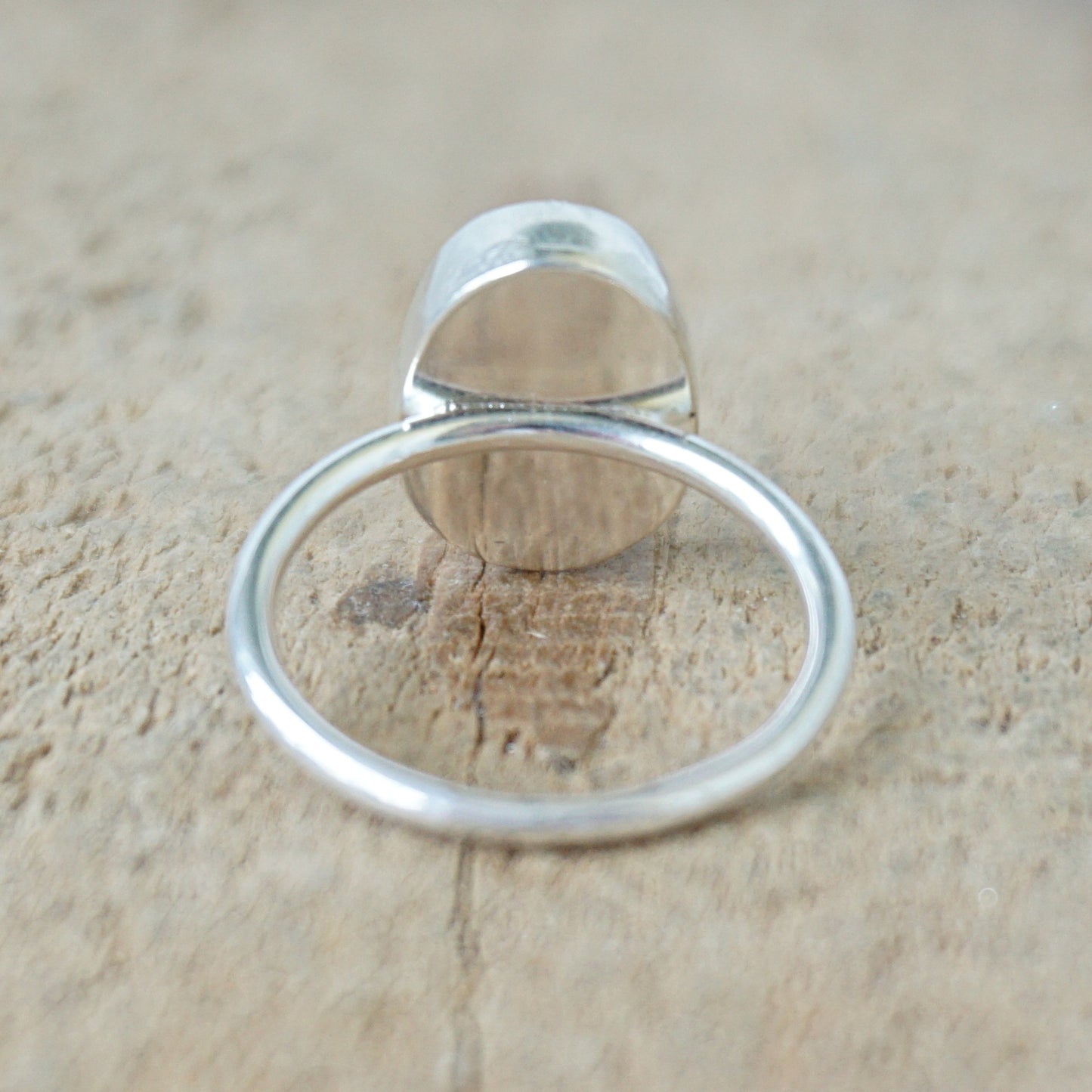 back view of a silver ring with a spotted stone on a wooden background