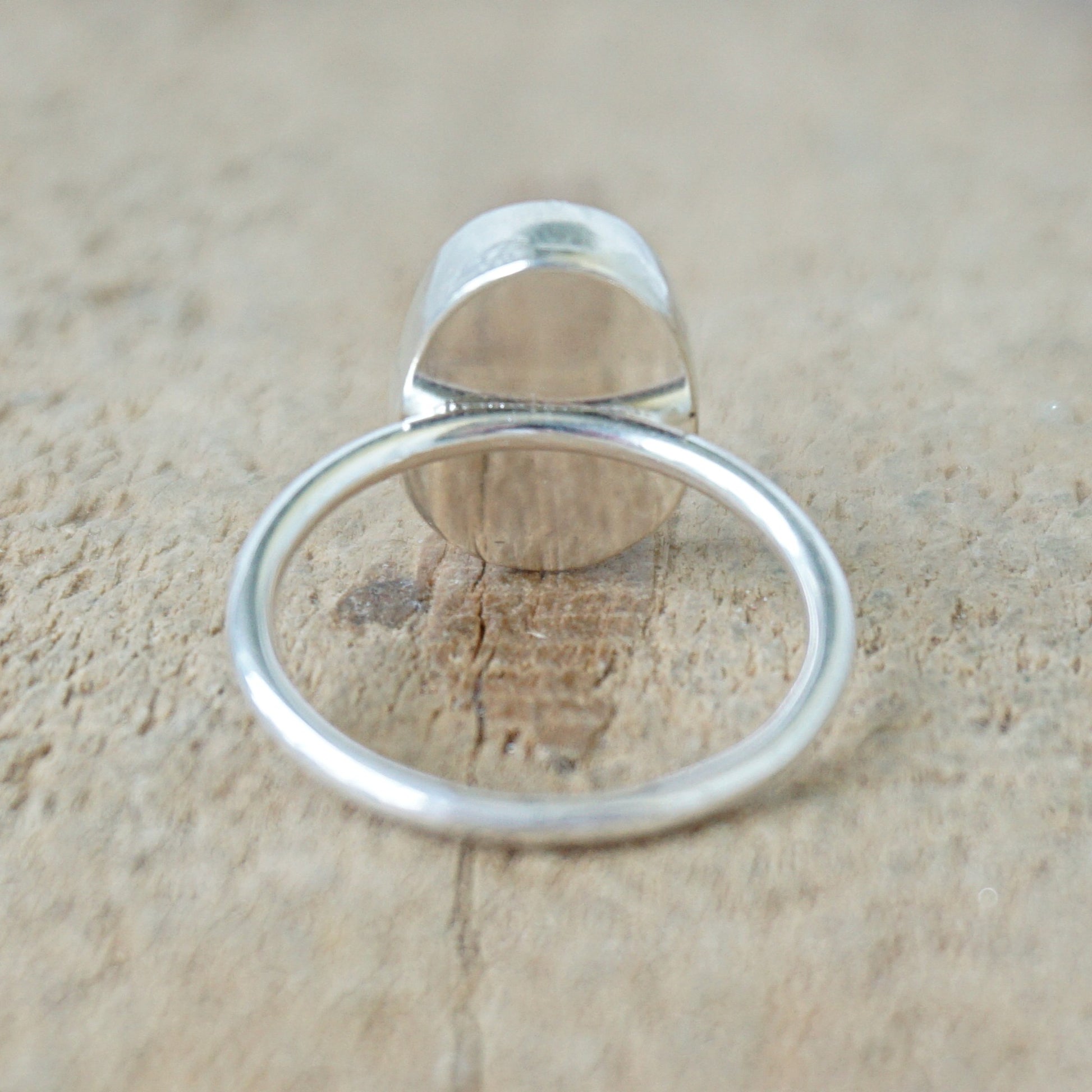 back view of a silver ring with a spotted stone on a wooden background