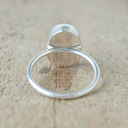 back view of a silver ring with a spotted stone on a wooden background