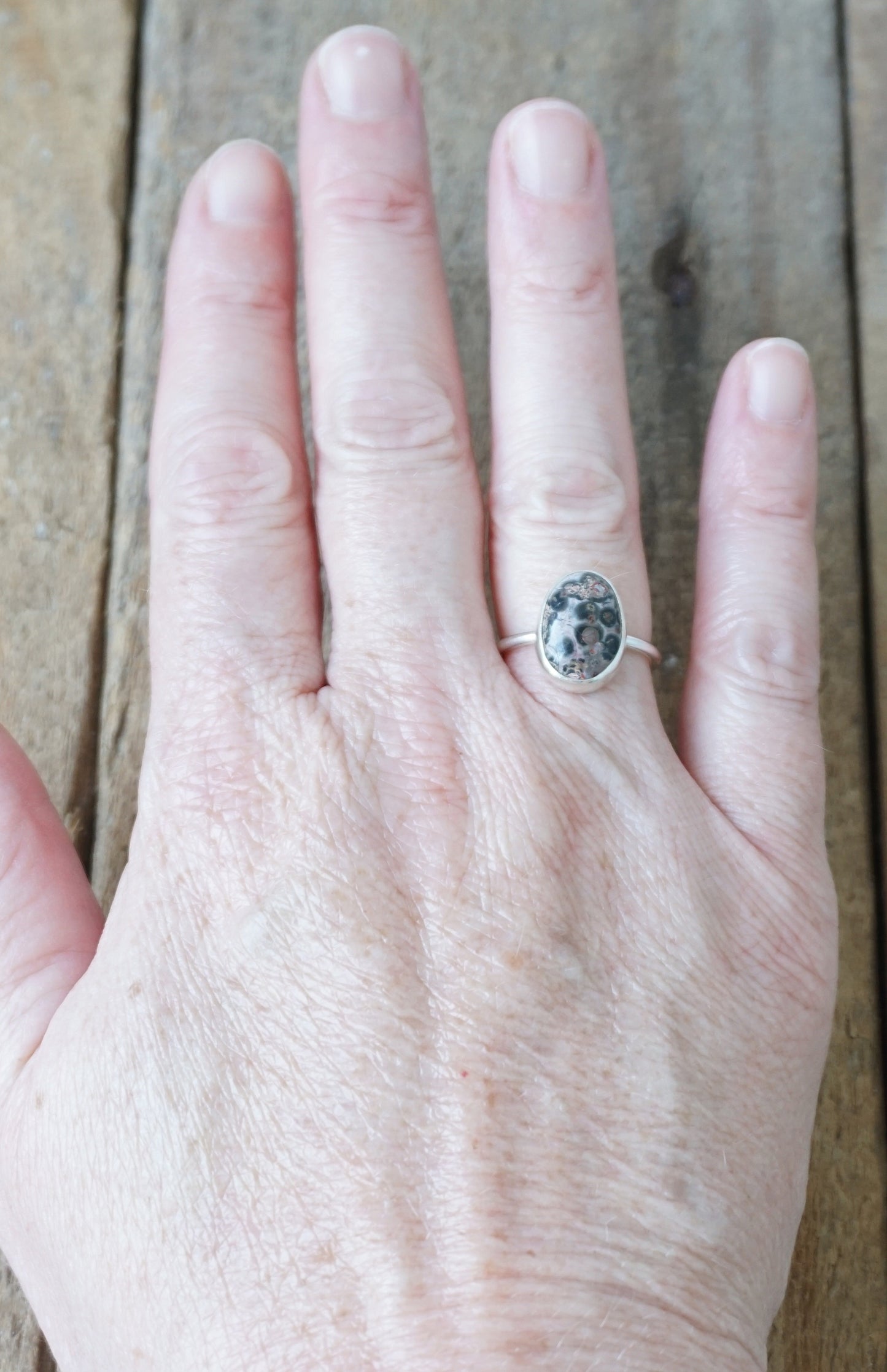 hand wearing a silver ring with a spotted stone on a wooden background