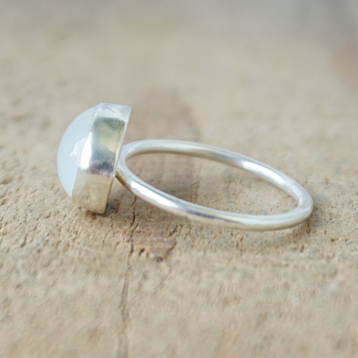 side view of a silver ring with a translucent stone on a wooden background