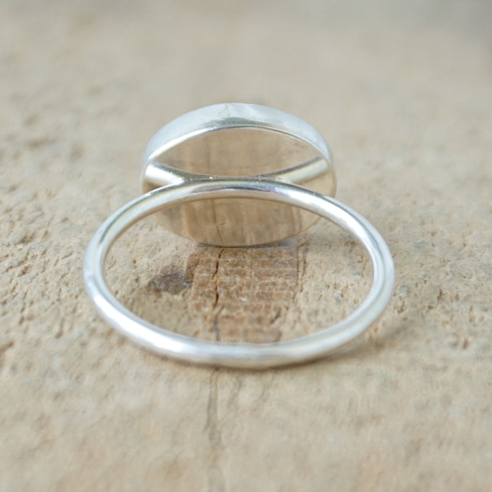 back view of a silver ring with a translucent stone on a wooden background