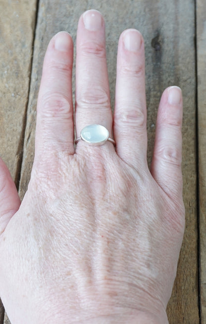 hand wearing a silver ring with a translucent stone on a wooden background