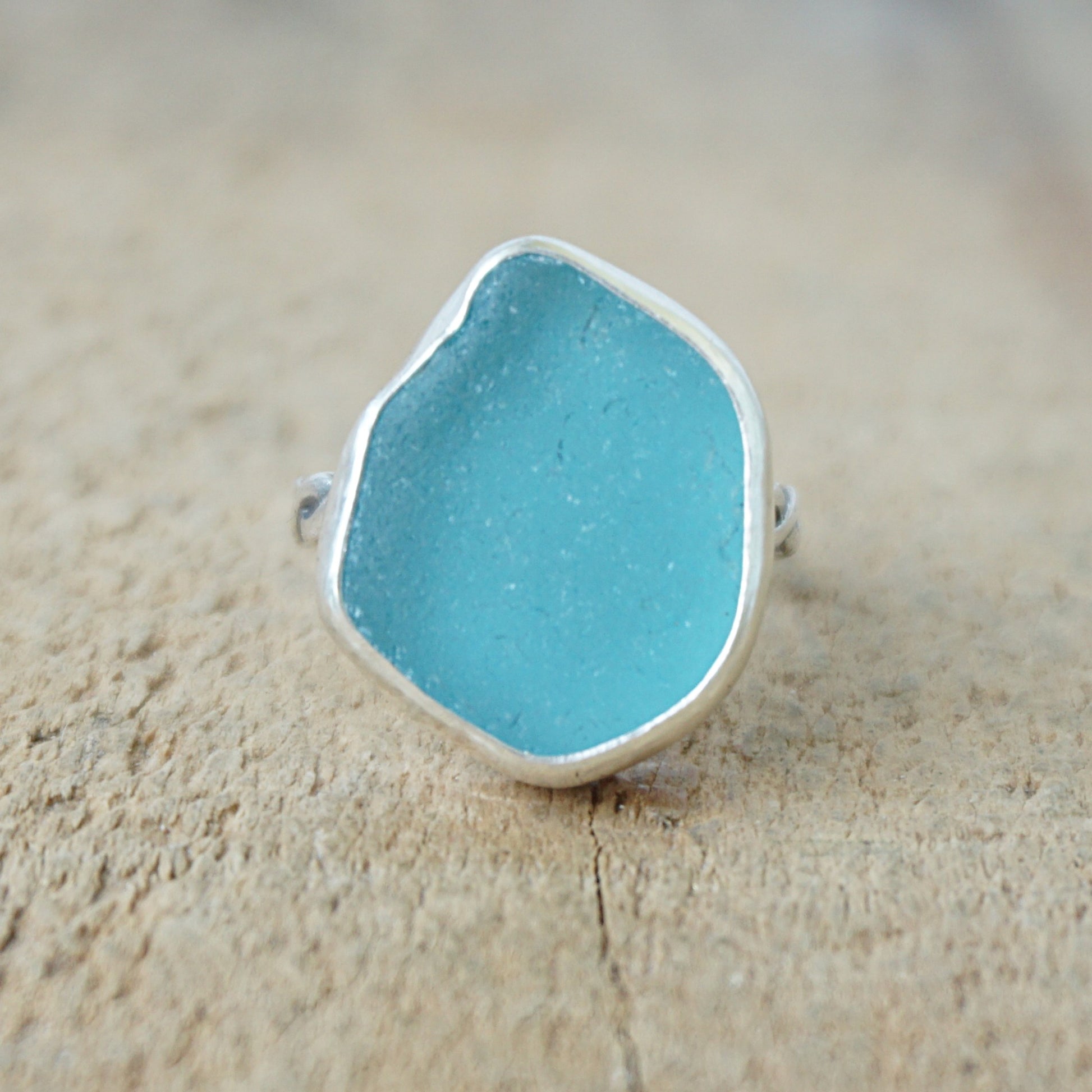 Teal sea glass ring with silver band on a wooden surface