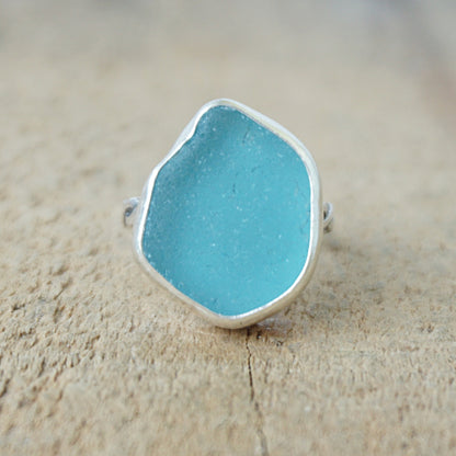 Teal sea glass ring with silver band on a wooden surface