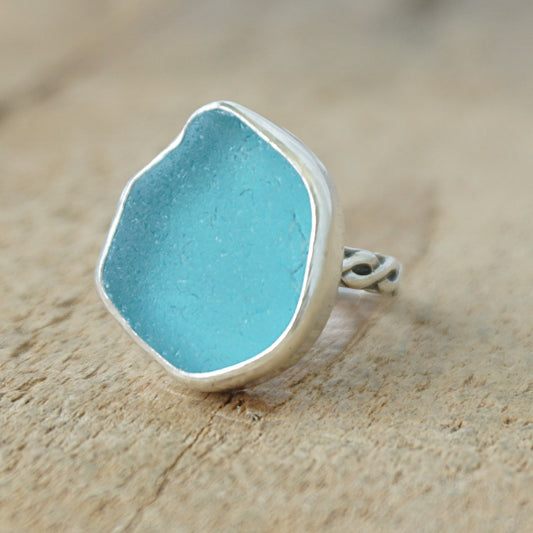 Teal sea glass ring with silver band on a wooden surface