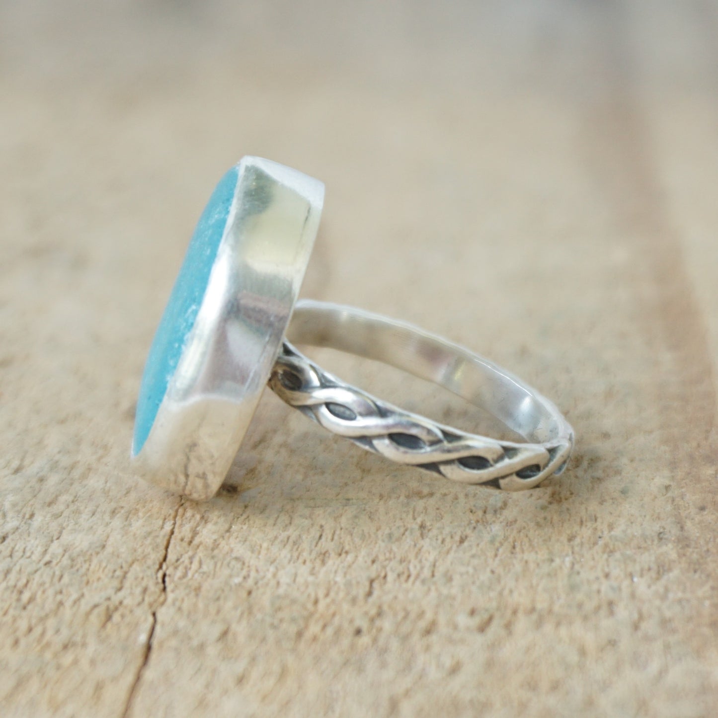 Teal sea glass ring with silver band on a wooden surface