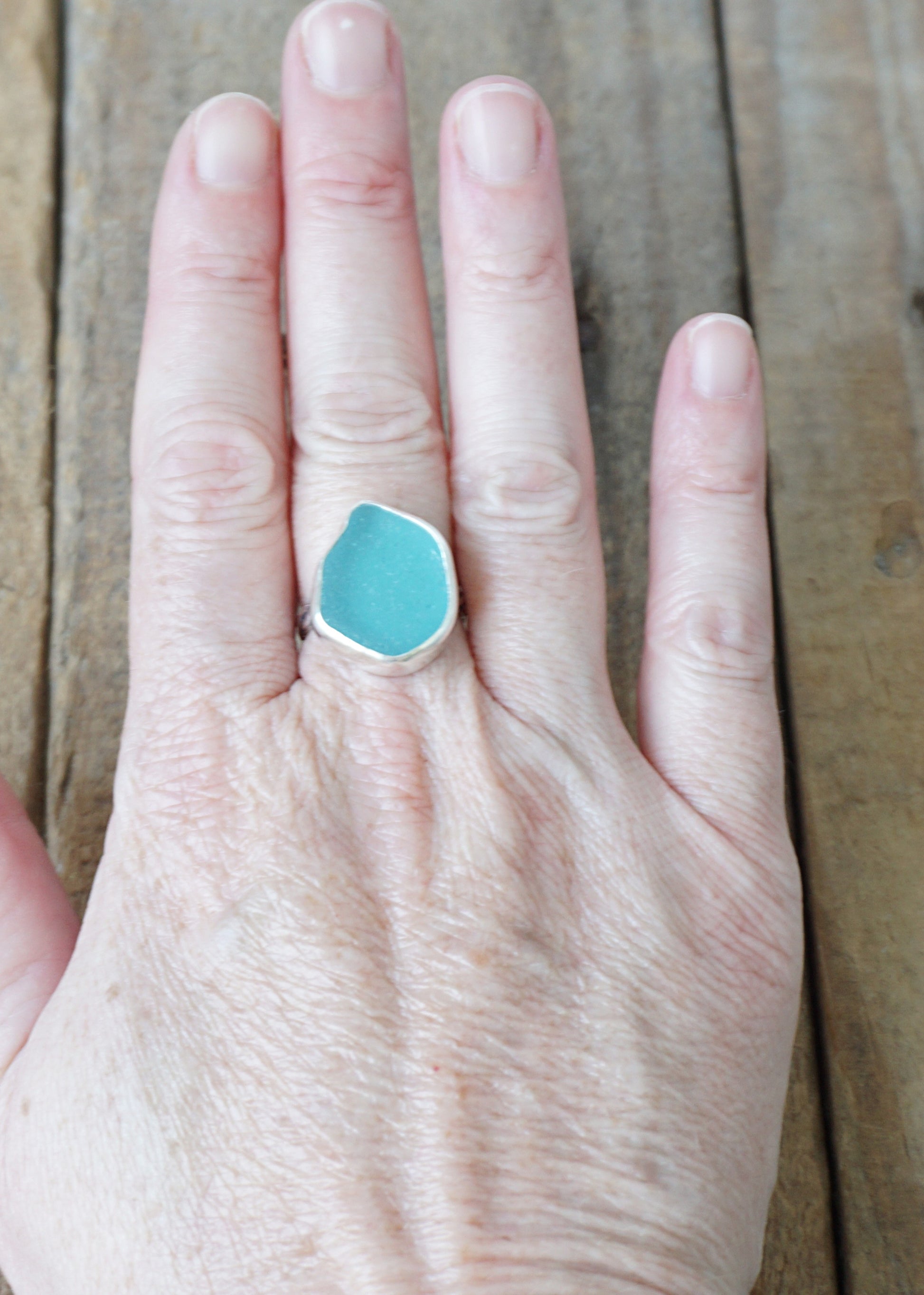Hand wearing a teal sea glass ring on a wooden surface