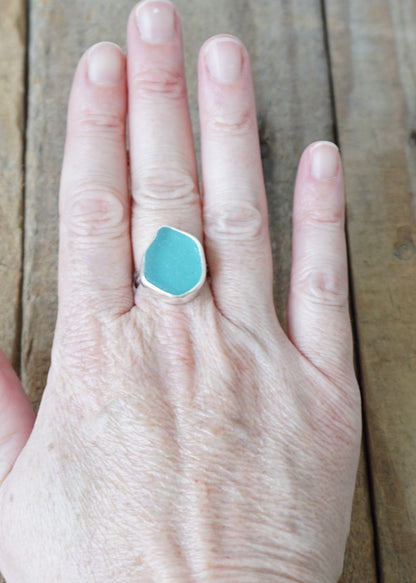 Hand wearing a teal sea glass ring on a wooden surface