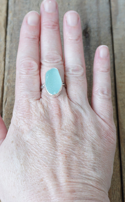 Hand wearing a ring with a light blue sea glass on a wooden surface