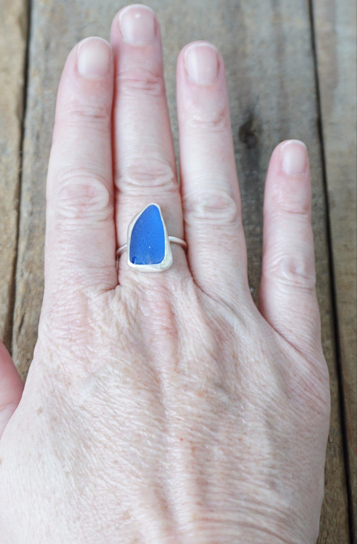 Hand wearing a blue ring on a wooden surface