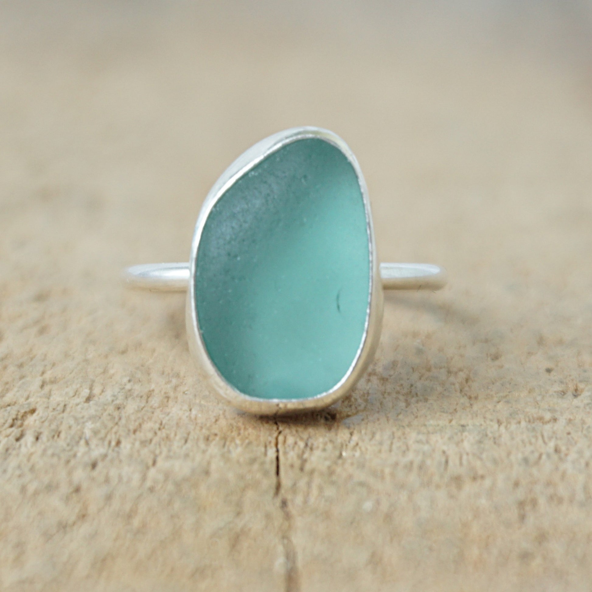 silver ring with teal sea glass on a wooden background