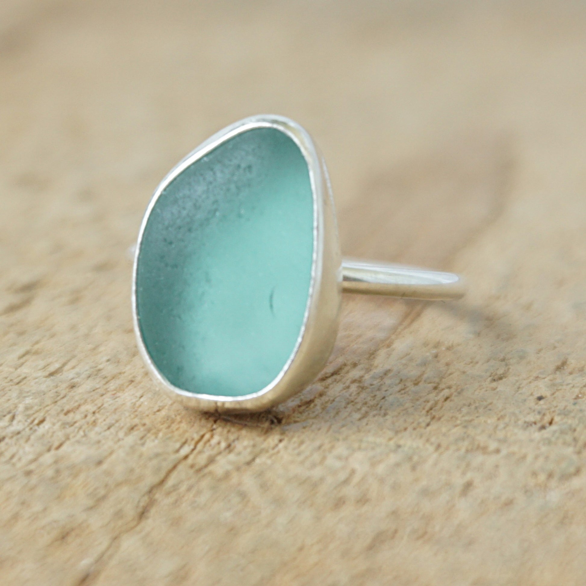 silver ring with teal sea glass on a wooden background