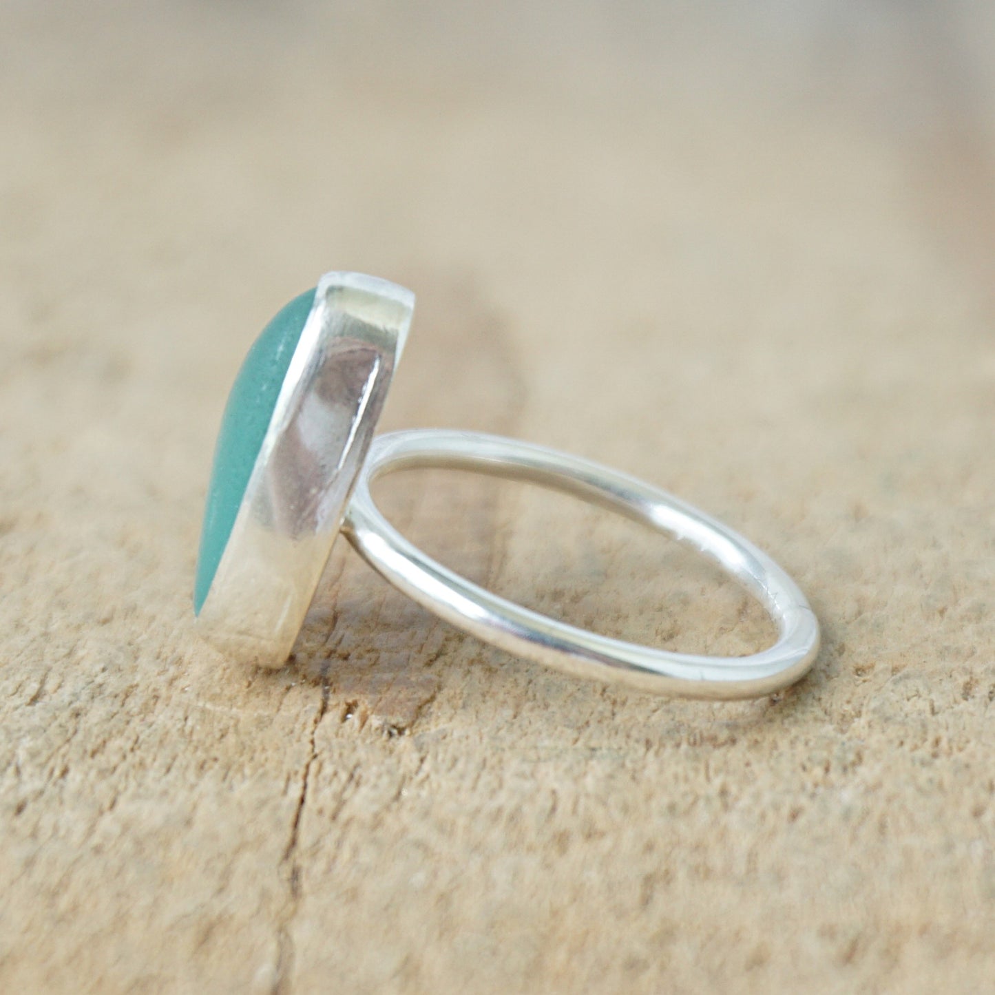 side view of a silver ring with teal sea glass on a wooden background