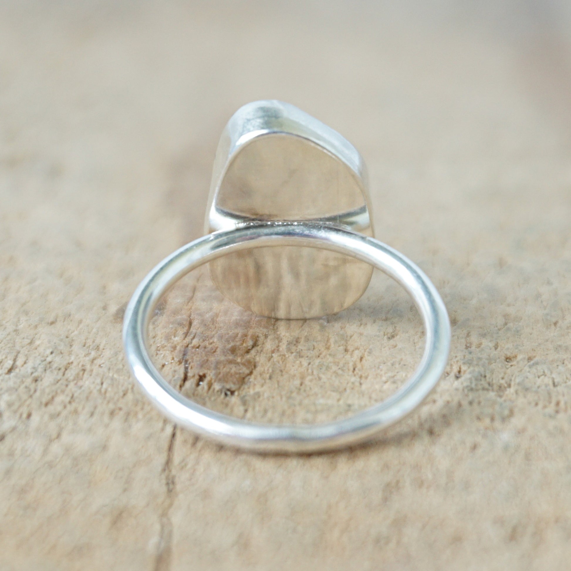 back view of a silver ring with teal sea glass on a wooden background