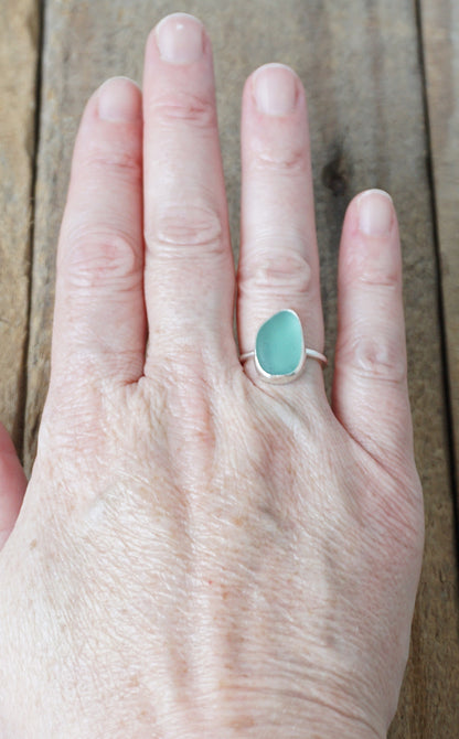 hand wearing a silver ring with teal sea glass on a wooden background
