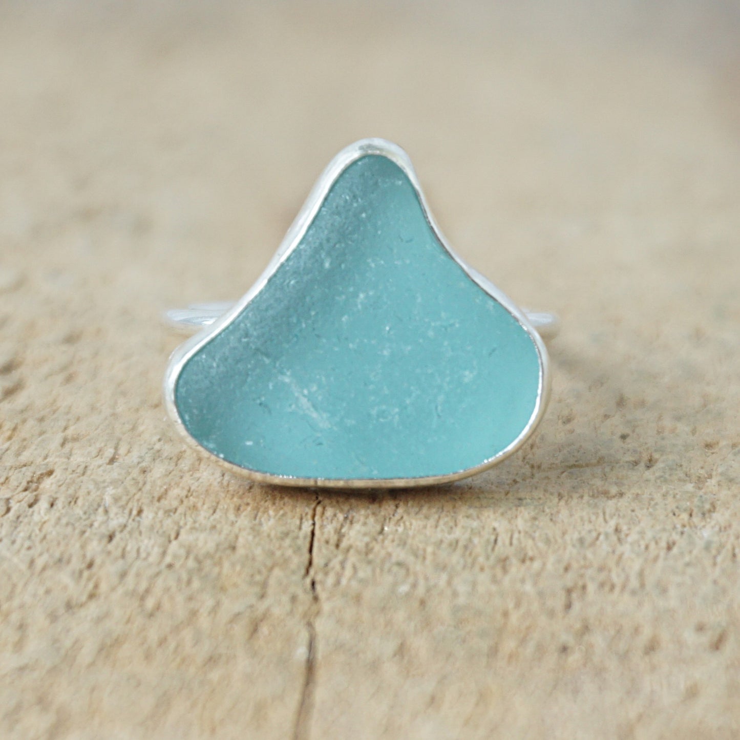 silver ring with teal sea glass on a wooden background