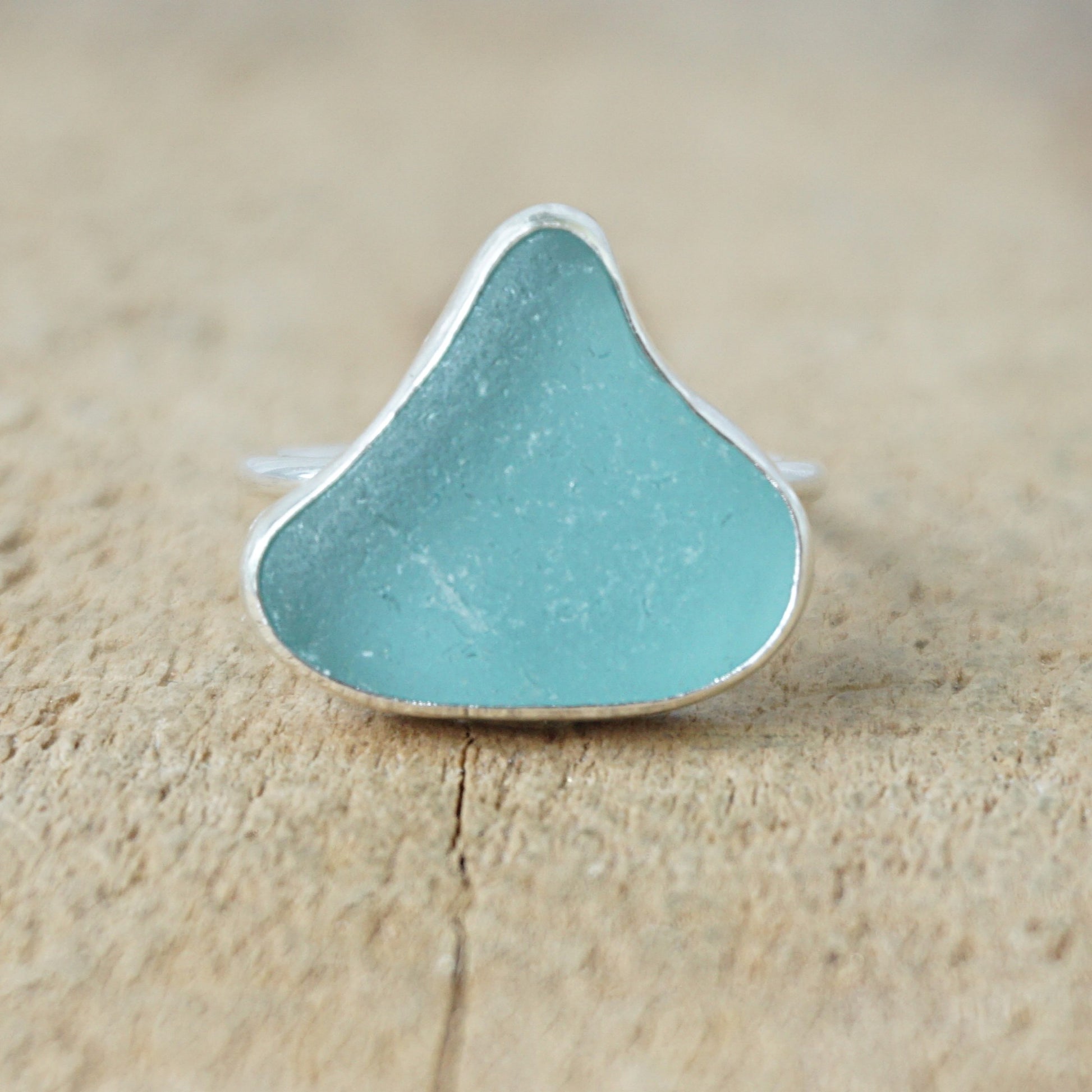 silver ring with teal sea glass on a wooden background