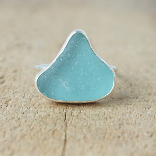 silver ring with teal sea glass on a wooden background